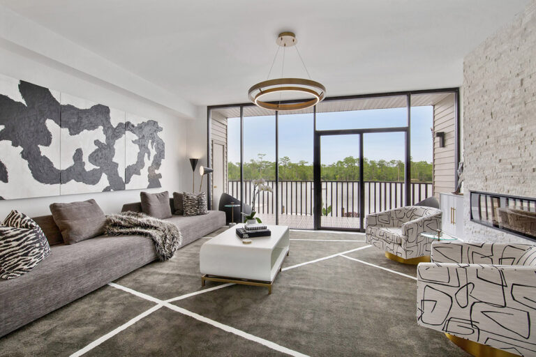 Riverfront townhome living room with a gray sofa, patterned armchairs, abstract artwork and full-height balcony windows